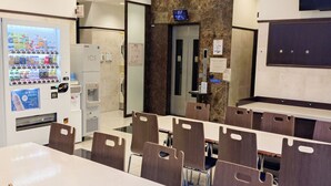 Ein Hotel-Speisesaal mit einem langen Tisch, mehreren Stühlen, einem Automaten, einem Eisspender und einem an der Wand befestigten Fernseher.