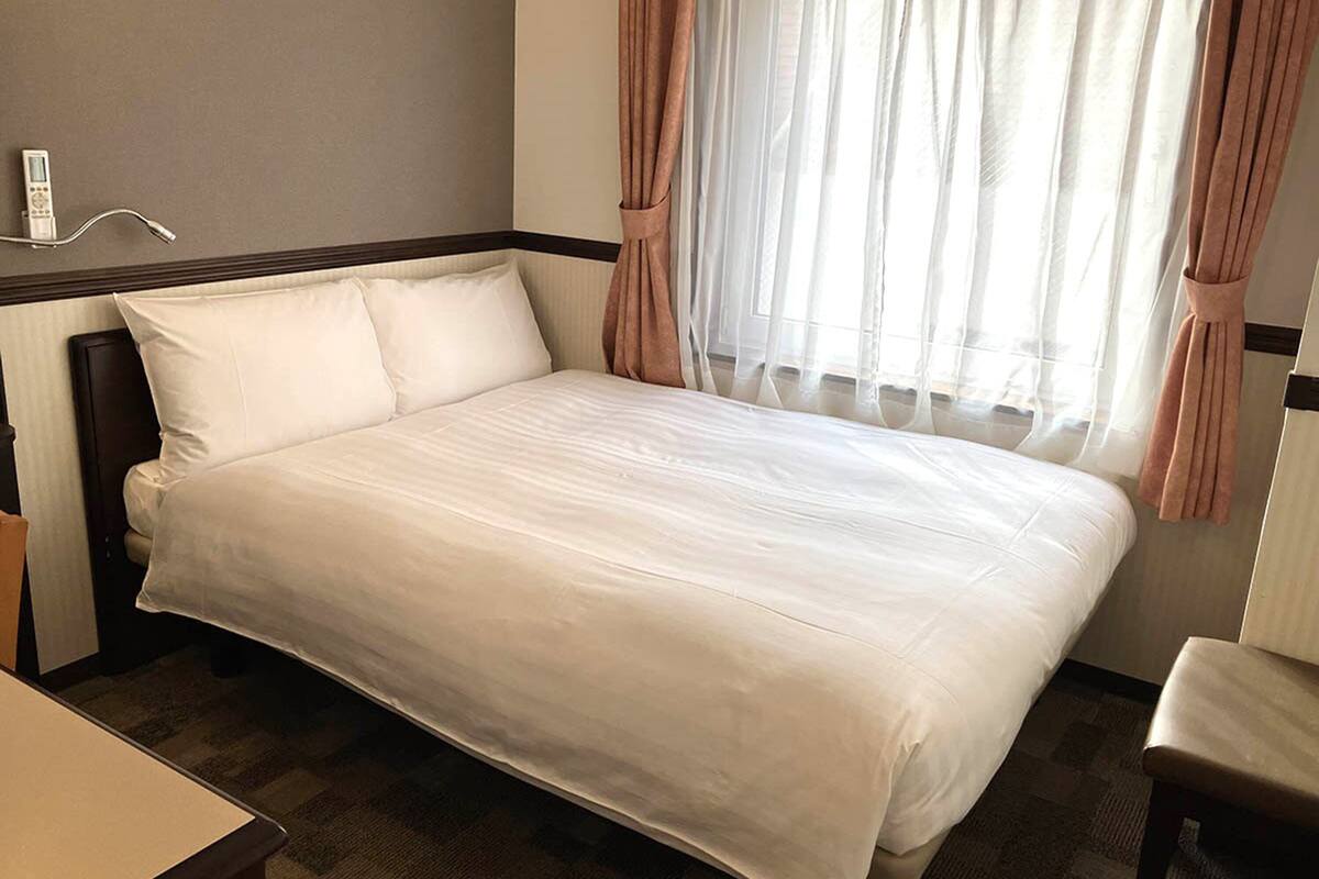 Ein ordentlich bezogenes Bett mit weißen Laken, ein Nachttisch und ein Stuhl.