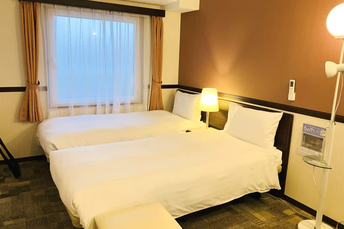 Une chambre d’hôtel avec deux lits, une table de chevet, une lampe et un téléviseur fixé au mur.