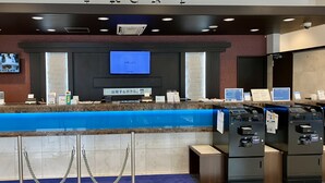 Een hotel receptie met een digitaal scherm, een balie met verschillende spullen en automaten.