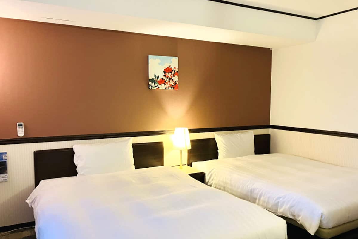 Une chambre d’hôtel avec deux lits, une table de chevet avec une lampe et un tableau au mur.