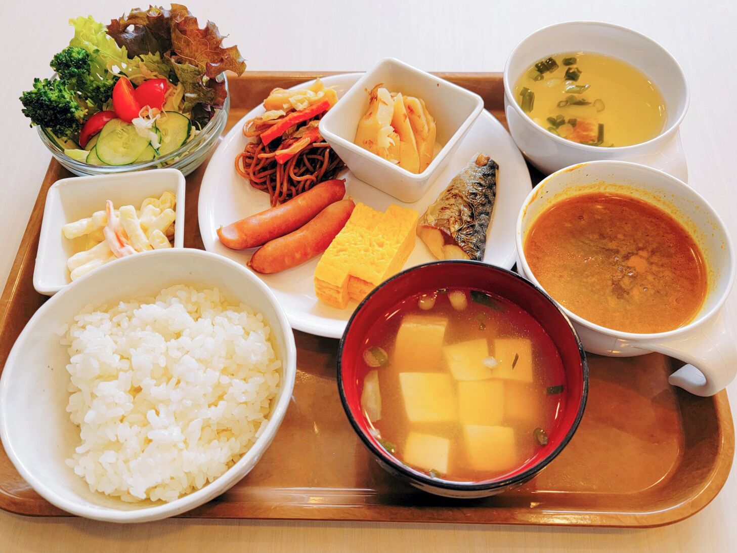 Una bandeja con diferentes platos, incluyendo arroz, fideos, una ensalada y varios cuencos de sopa.