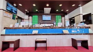 Una recepción de hotel con pantalla digital, zona de asientos y carteles informativos.
