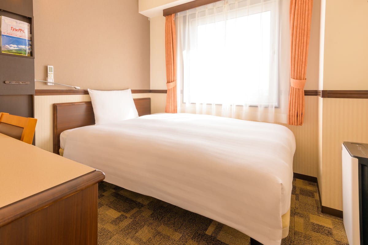 Ein Hotelzimmer mit Bett, Schreibtisch, Stuhl, einem Fenster mit Vorhängen und einem an der Wand montierten Telefon.