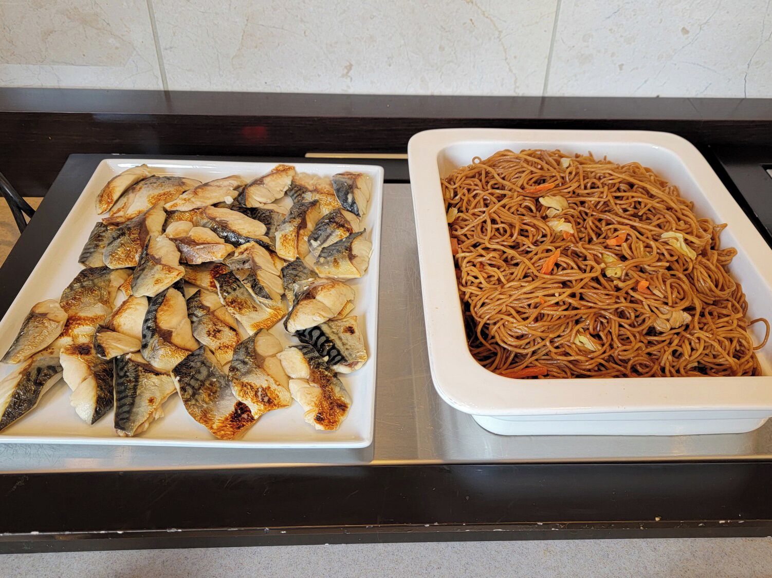Dos platos sobre una mesa: uno con pescado a la parrilla y otro con fideos.