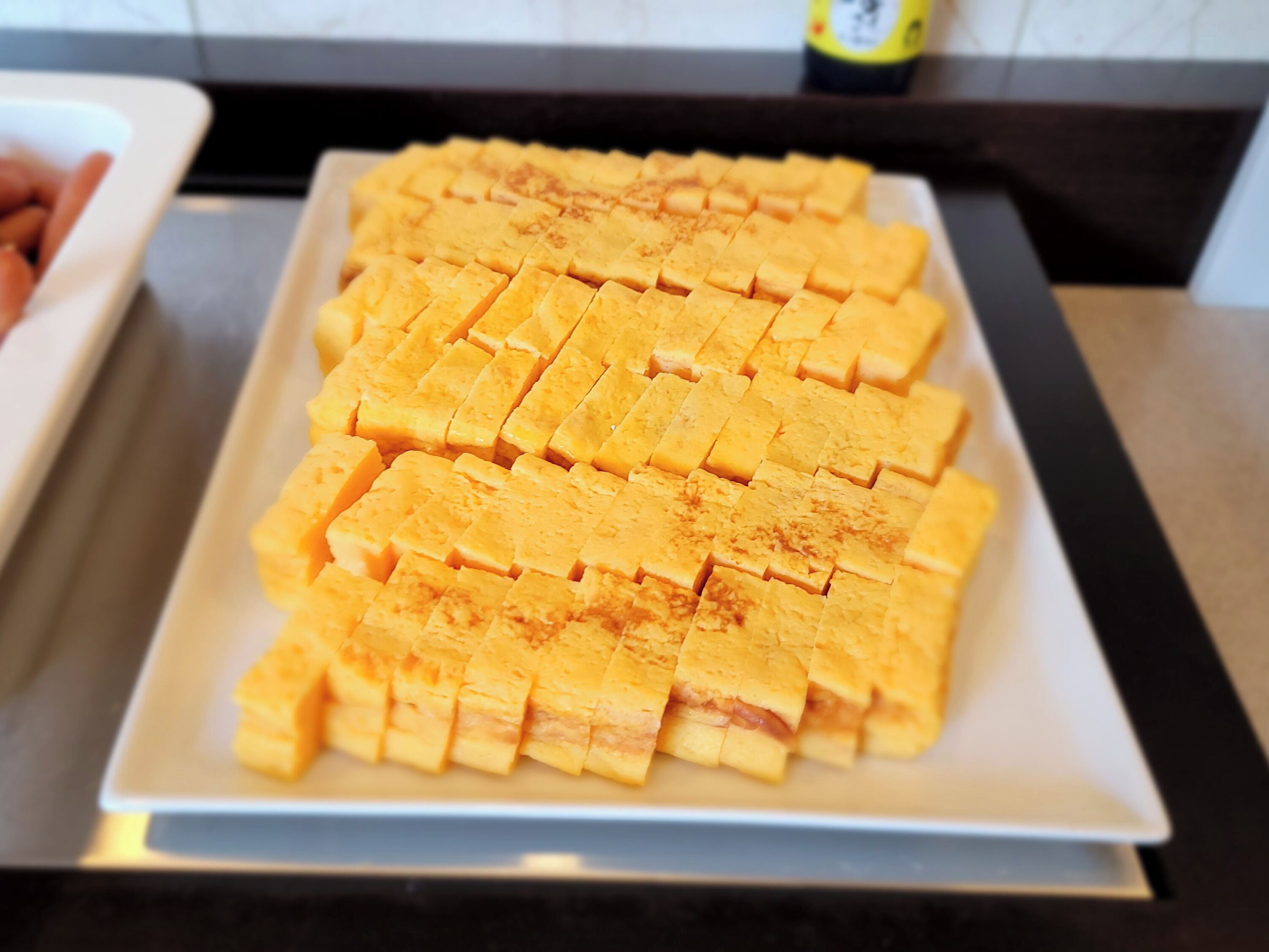 A white rectangular plate with neatly arranged yellow rectangular pieces, possibly food items, on a kitchen counter.