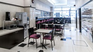 A modern restaurant with a clean, minimalist design, featuring a central dining area with tables and chairs, a coffee station, and a large window providing natural light. - Toyoko Inn Kintetsu Nara Ekimae (Nara)