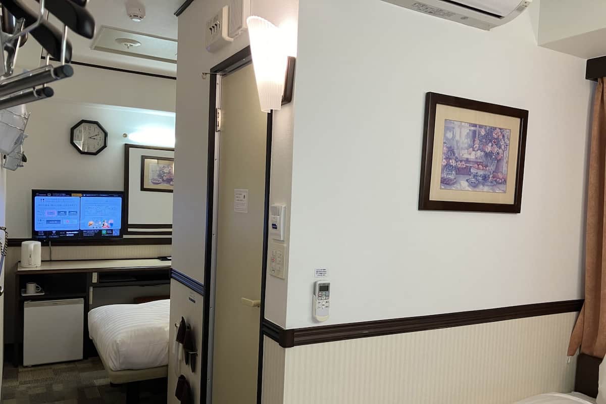A hotel room with a bed, a desk with a computer, a clock, and a framed picture on the wall.