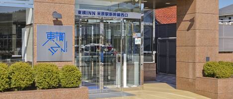 Entrada de hotel con puerta de vidrio, letrero y rampa accesible para sillas de ruedas.