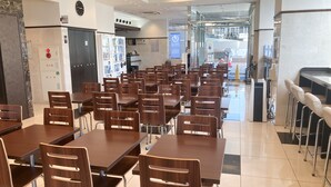 A cafeteria with multiple wooden tables and chairs, a clock on the wall, and a vending machine. - Toyoko Inn Maibara Station Shinkansen Nishi (Maibara)