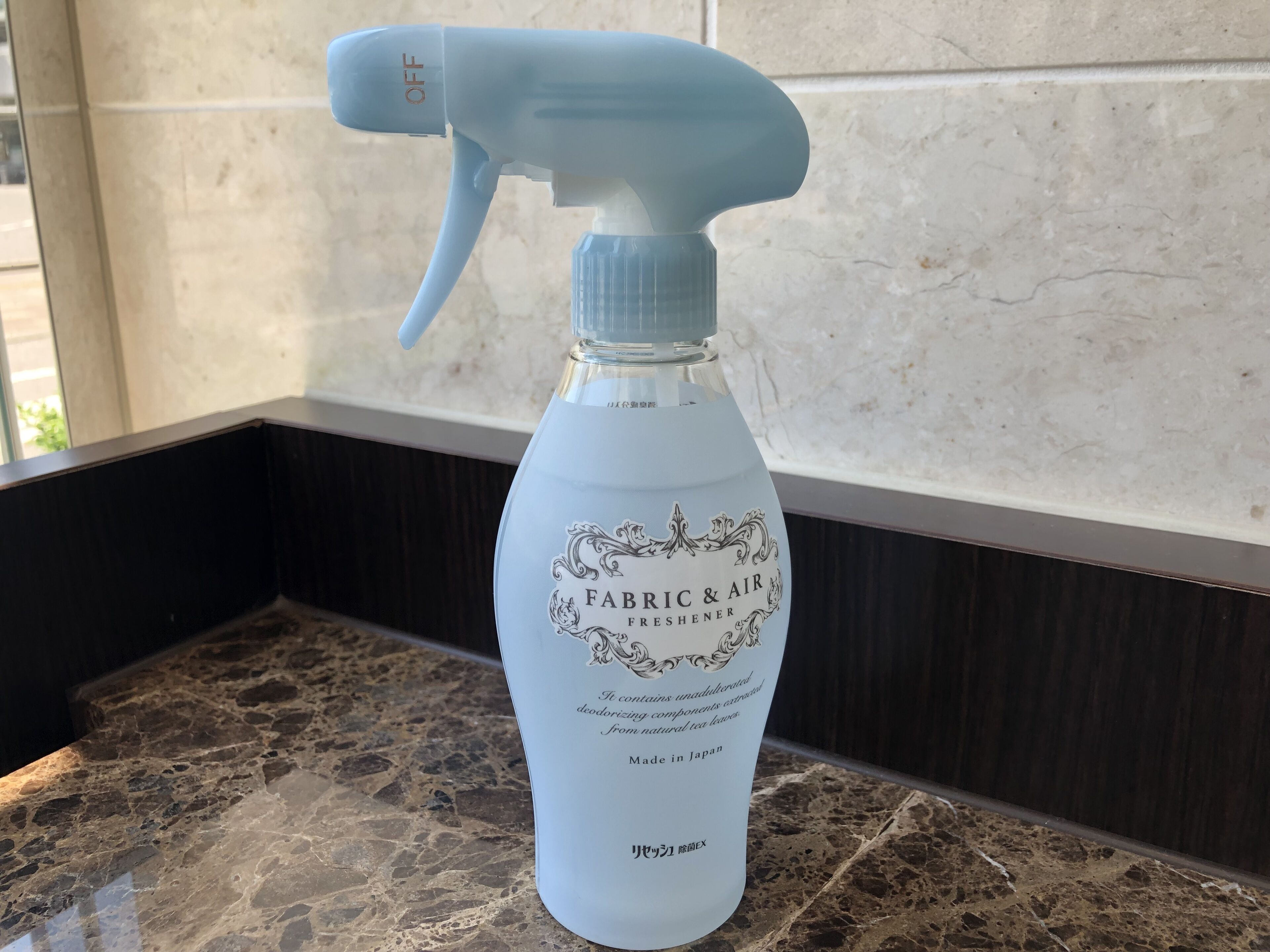 A spray bottle labeled "FABRIC & AIR FRESHENER" on a marble countertop.