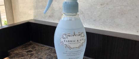 Un atomizador etiquetado como "FABRIC & AIR FRESHENER" sobre una encimera de mármol.