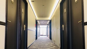 A hotel hallway with carpeted floors, dark wooden doors, and a bright ceiling light. - Toyoko Inn Maibara Station Shinkansen Nishi (Maibara)