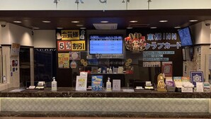 A hotel reception area with a digital display, promotional signs, and a counter with various items.