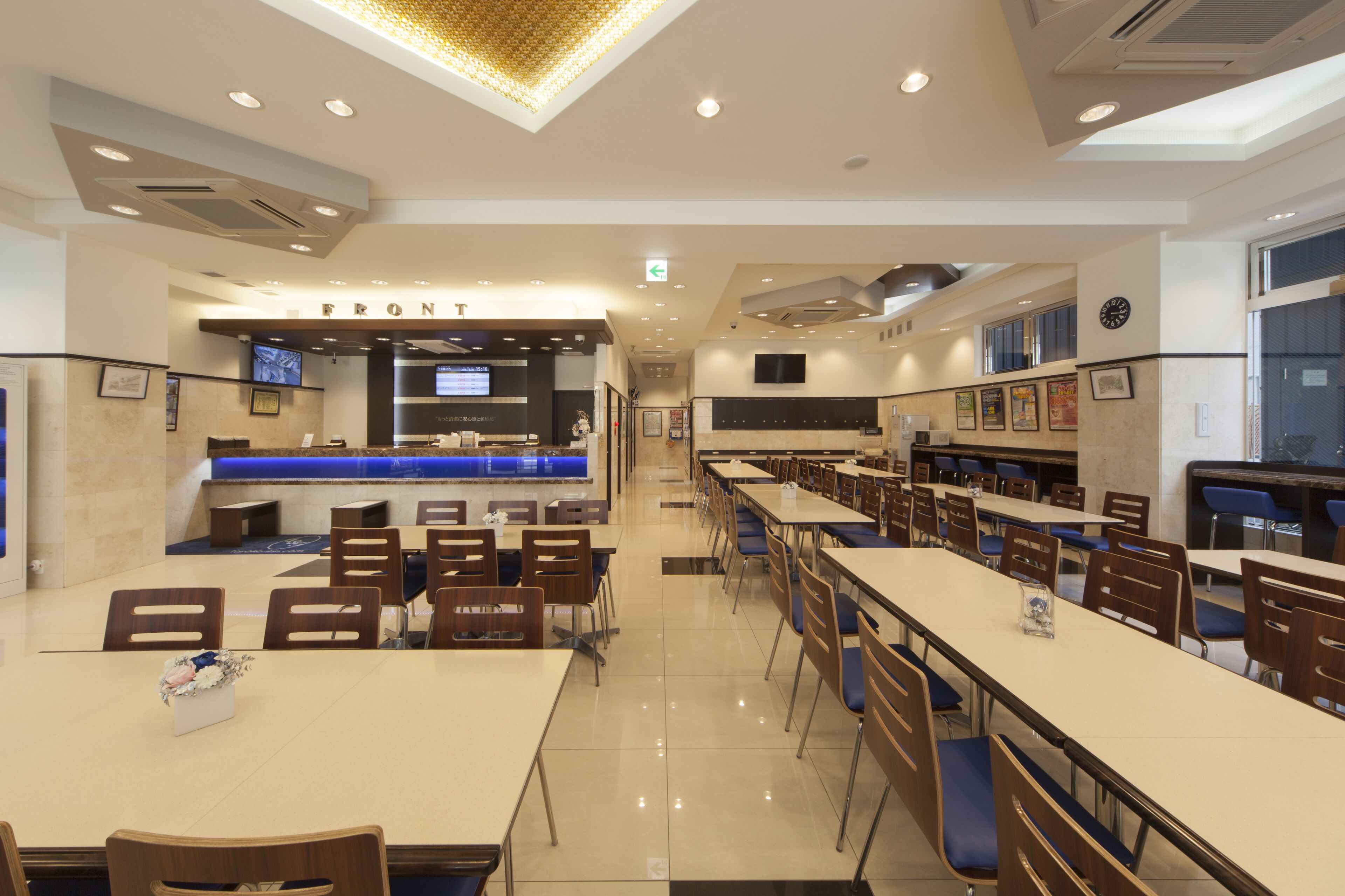 Una cafeteria àmplia amb taules i cadires llargues, una barra amb pantalla digital i quadres emmarcades a les parets.