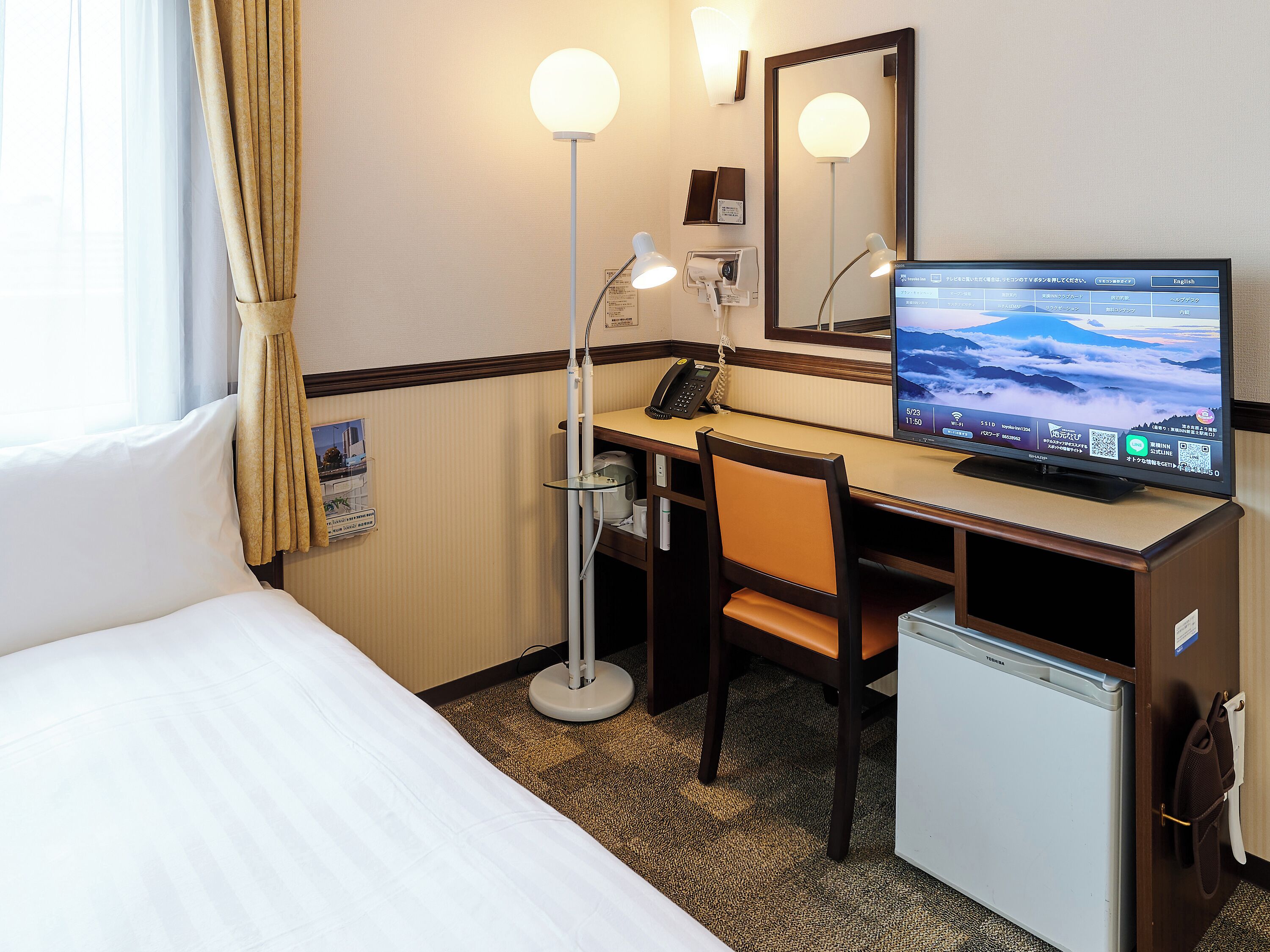 Une chambre d’hôtel équipée d’un lit, d’un bureau, d’une chaise, d’une lampe de bureau et d’un petit réfrigérateur.