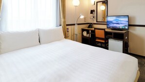 Una habitación de hotel con una cama grande, un escritorio con computadora, una lámpara y un televisor.