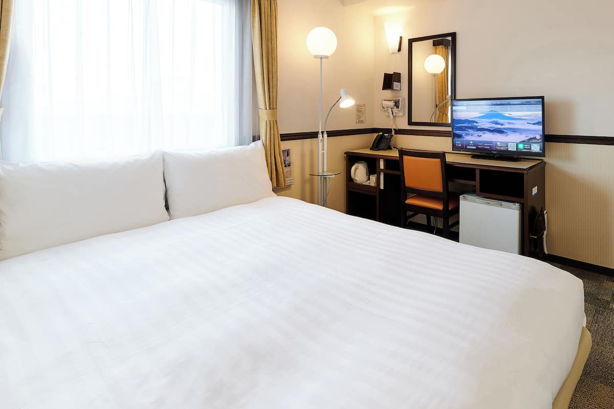 A hotel room with a large bed, a desk with a computer, a lamp, and a TV.