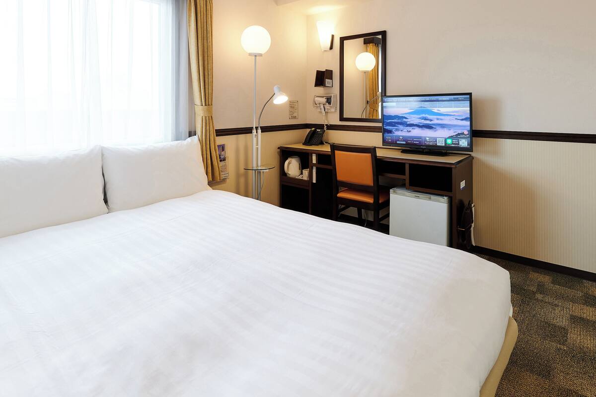 Una habitación de hotel con una cama grande, un escritorio con ordenador, una lámpara de escritorio y un espejo.