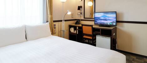 A hotel room with a large bed, a desk with a computer, a desk lamp, and a mirror.