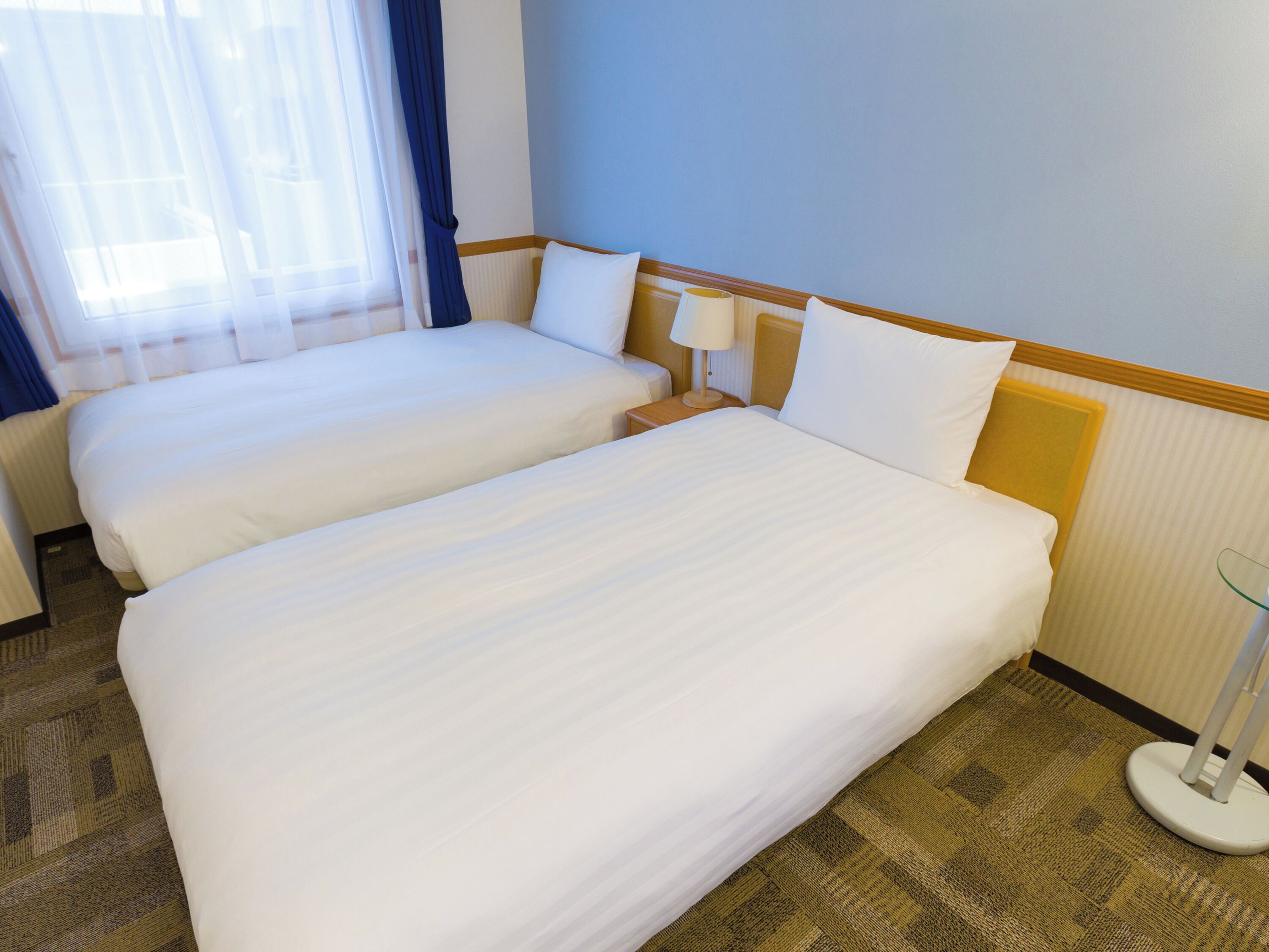 Una habitación de hotel con dos camas, una mesita de noche, una lámpara y una ventana con cortinas.