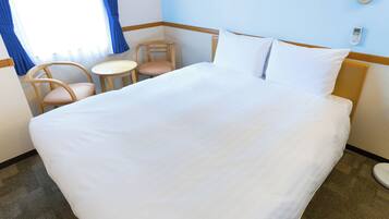 A hotel room with a large bed, two chairs, a small table, and a thermostat on the wall.