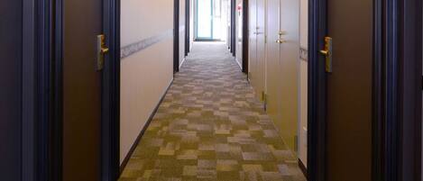 Pasillo de hotel con pisos alfombrados, puertas a ambos lados y vista a otra habitación al fondo.