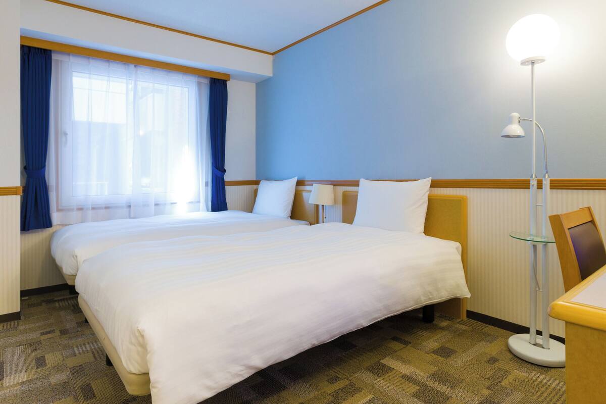 Une chambre d’hôtel avec un grand lit, une table de chevet, une lampe et une fenêtre avec des rideaux.