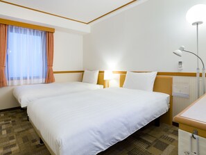 Two single beds with bedside tables and lamps, set in a clean and simple room with a window and carpeted floor.