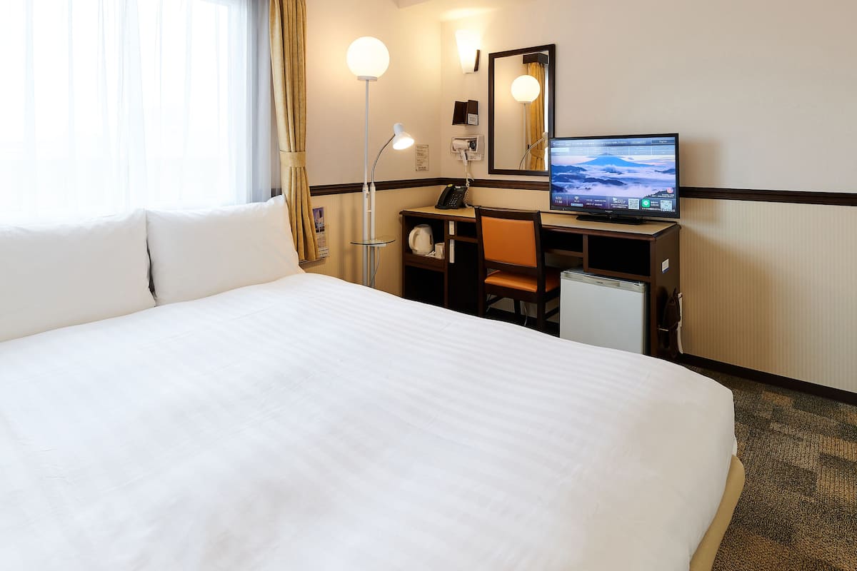 A hotel room with a large bed, a desk with a computer, a desk lamp, a telephone, and a mirror.