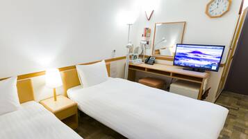 A hotel room with two single beds, a desk with a computer, a clock, and a mirror.