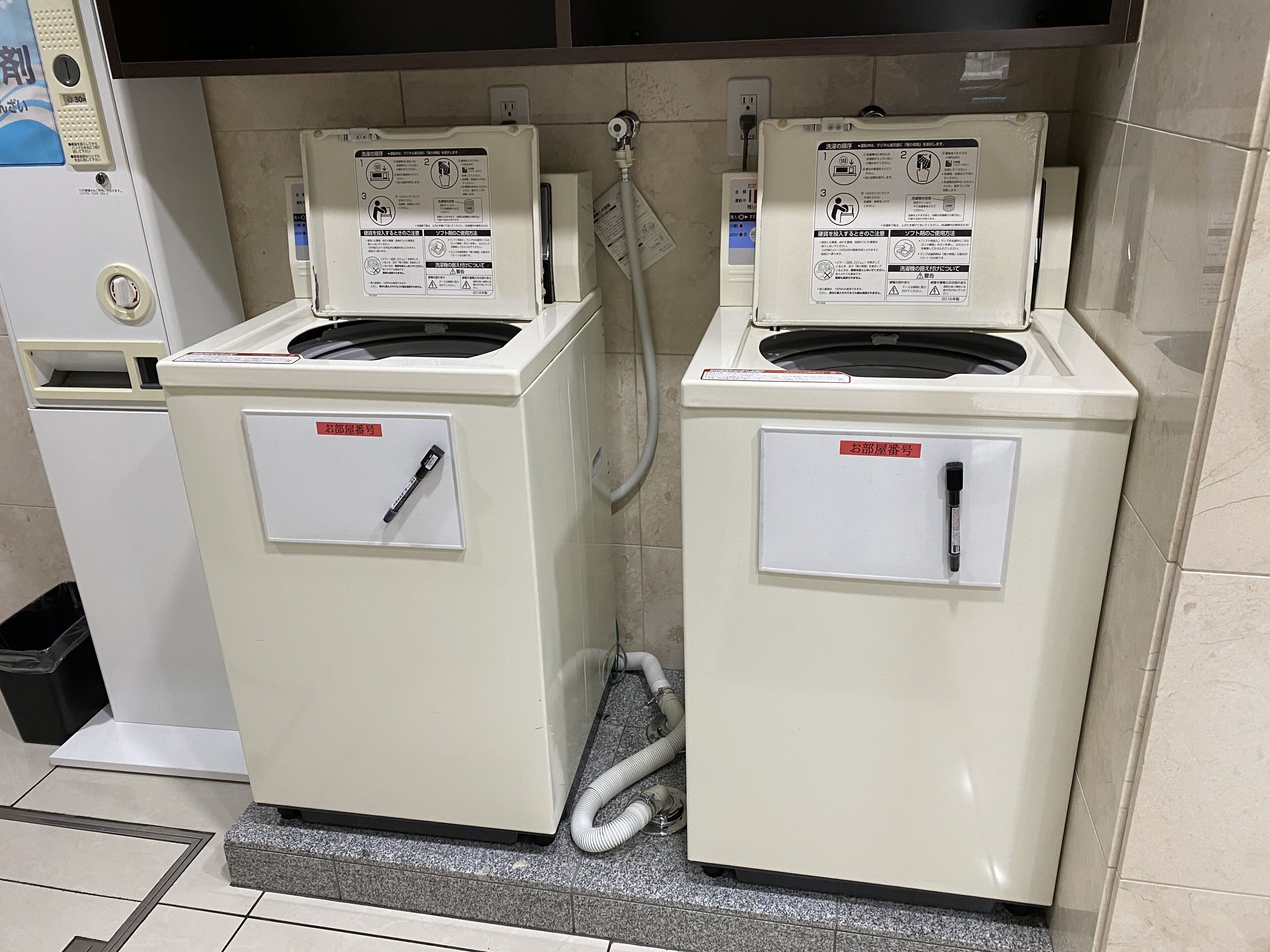Deux machines à laver à chargement frontal, installées dans un espace commercial, avec des instructions clairement visibles et une étiquette d’entretien.