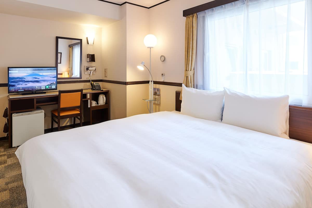 A hotel room with a bed, desk, chair, television, and a window with curtains.
