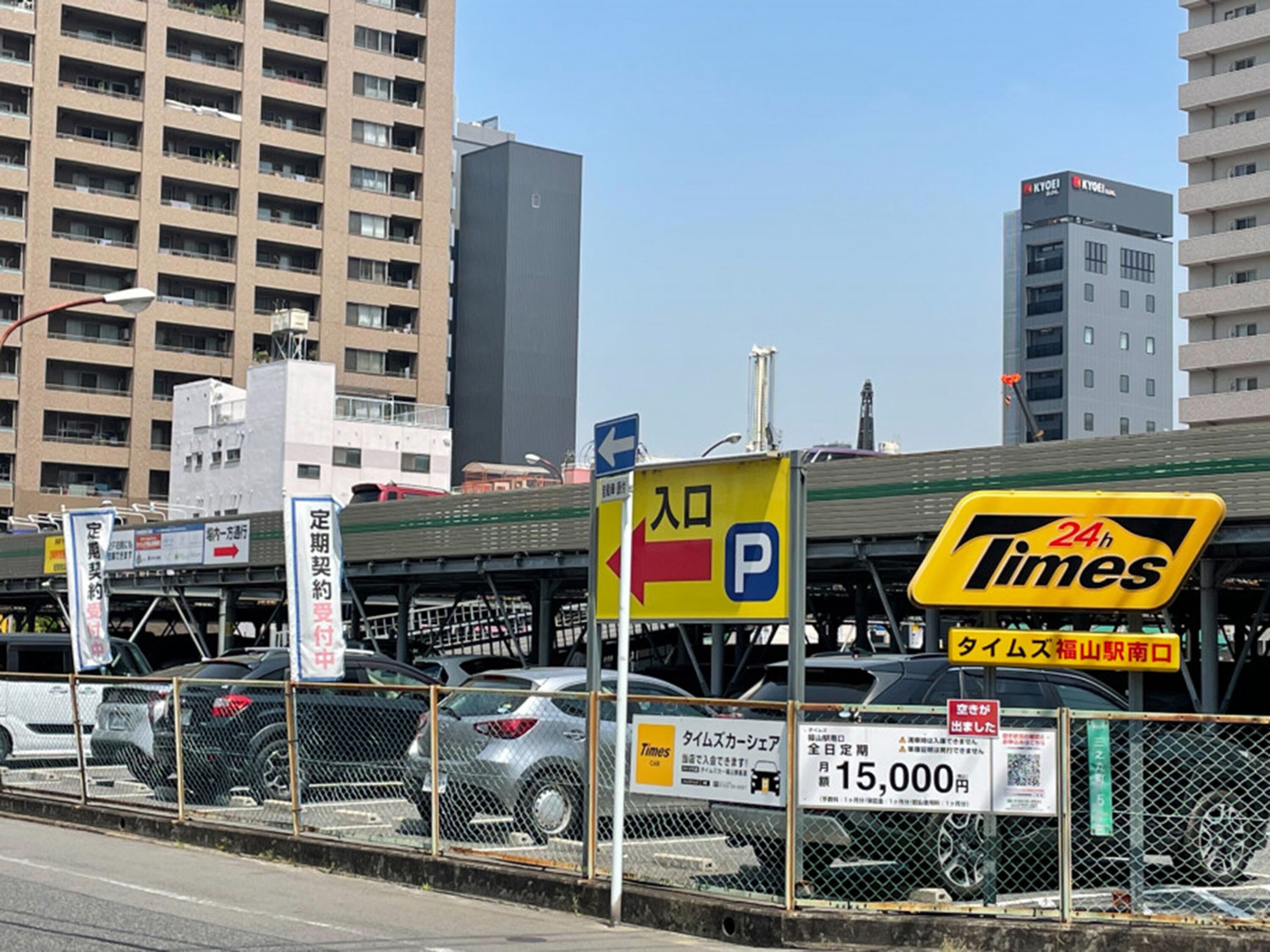 A parking lot with cars, a 24-hour Times sign, and a building in the background.