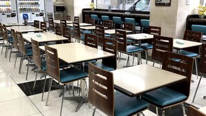 A cafeteria with multiple tables and chairs, vending machines, and a counter with a menu.