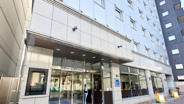 A modern hotel entrance with glass doors, a visible reception area, and a clear view of the interior through the glass.