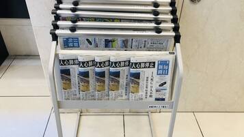 Un kiosque à journaux proposant de nombreux journaux et magazines, un présentoir métallique doté de boutons noirs et un sol carrelé.