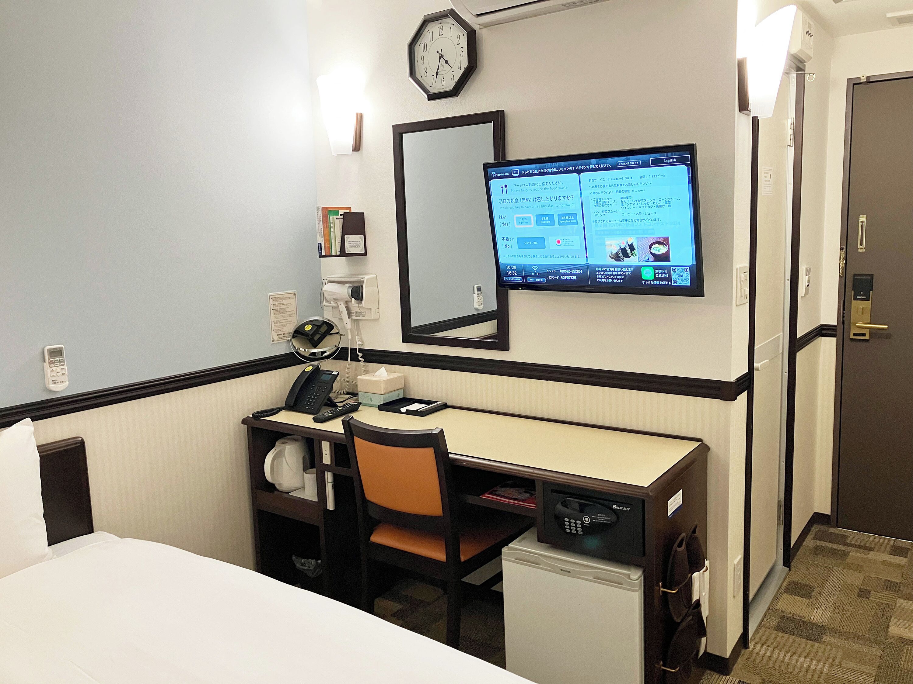 Een hotelkamer met een bureau, stoel, bed en een kleine koelkast.