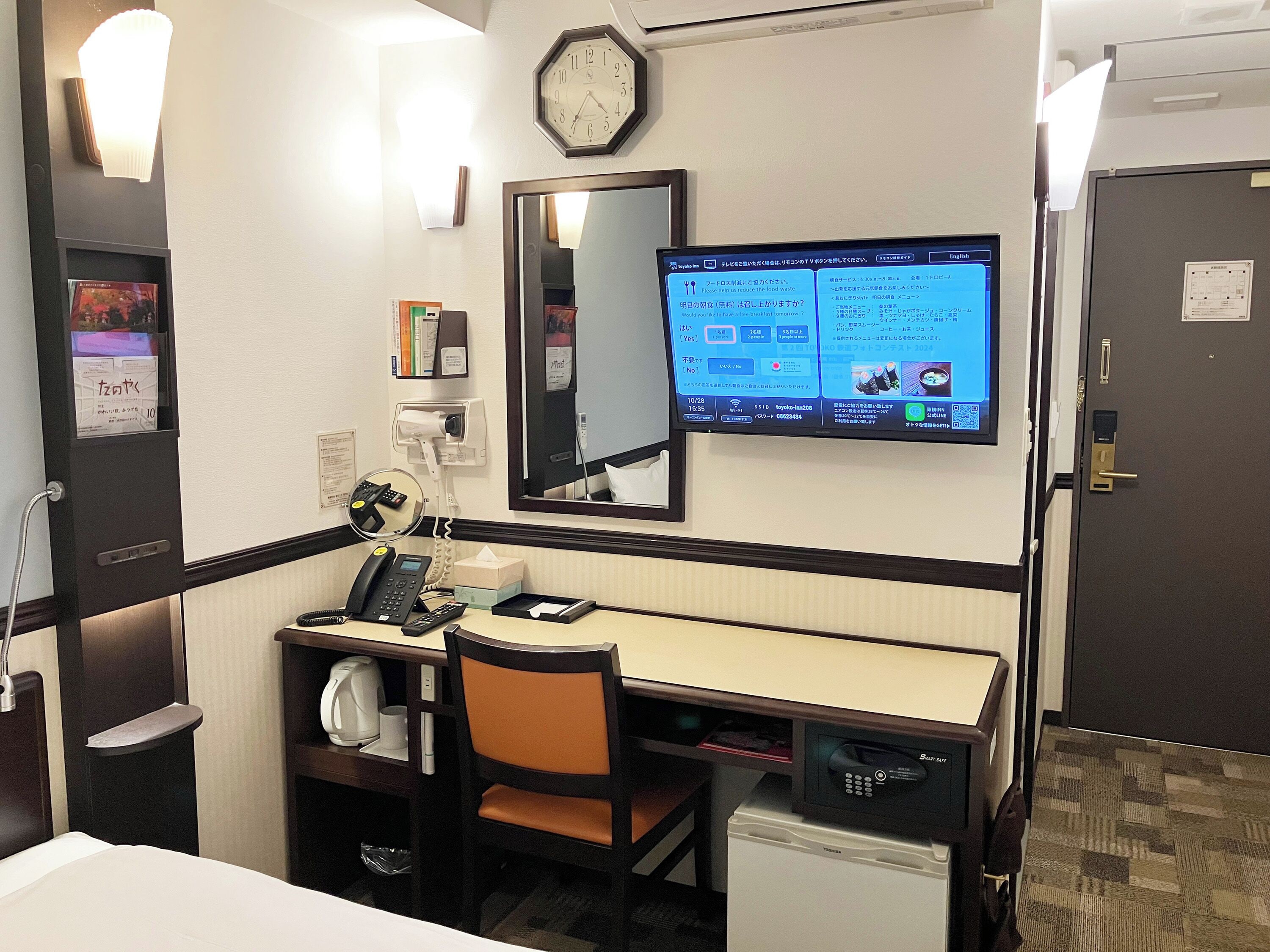 A hotel room with a desk, chair, and a television displaying a menu.