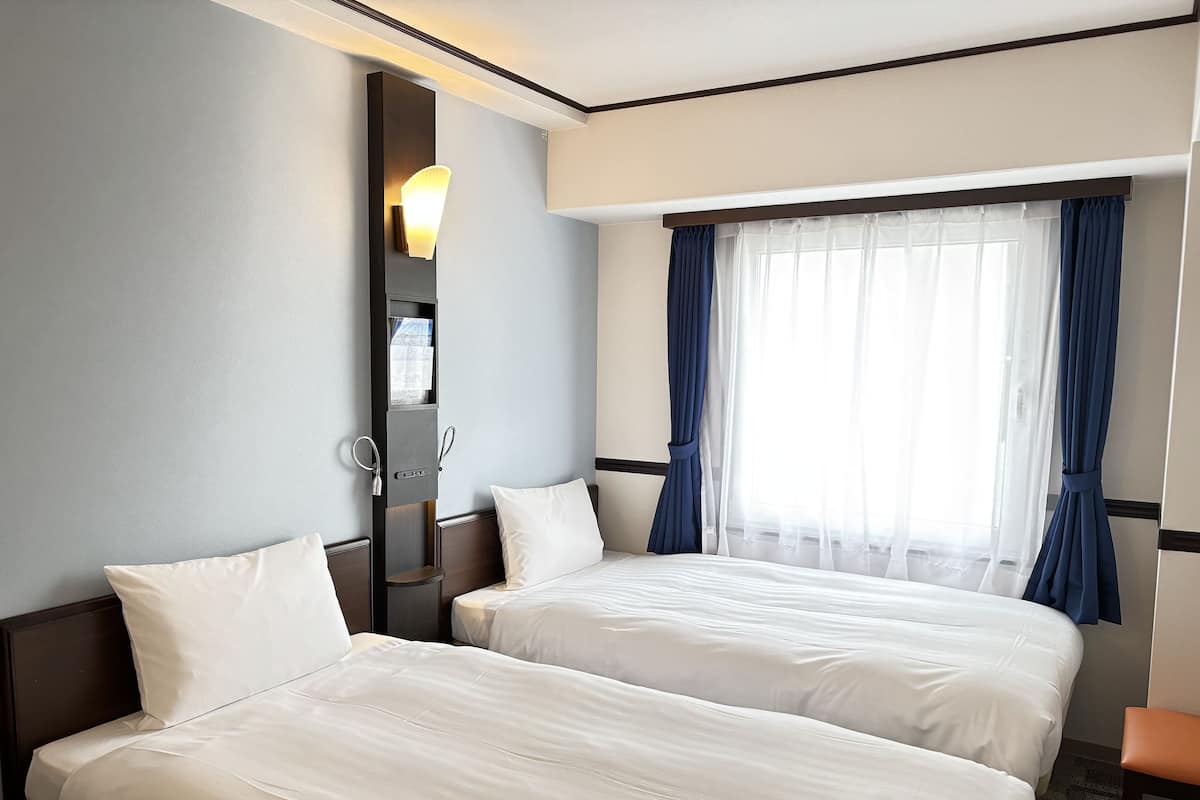 Quarto de hotel com duas camas, um espelho grande e uma janela com cortinas azuis.