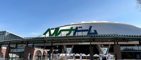 Un estadio con un cartel grande verde y blanco, una entrada cubierta y un área de control de entradas.