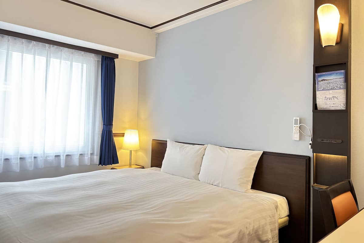 Quarto de hotel com uma cama grande, uma mesa de cabeceira com abajur, um telefone na parede e um porta-retrato.