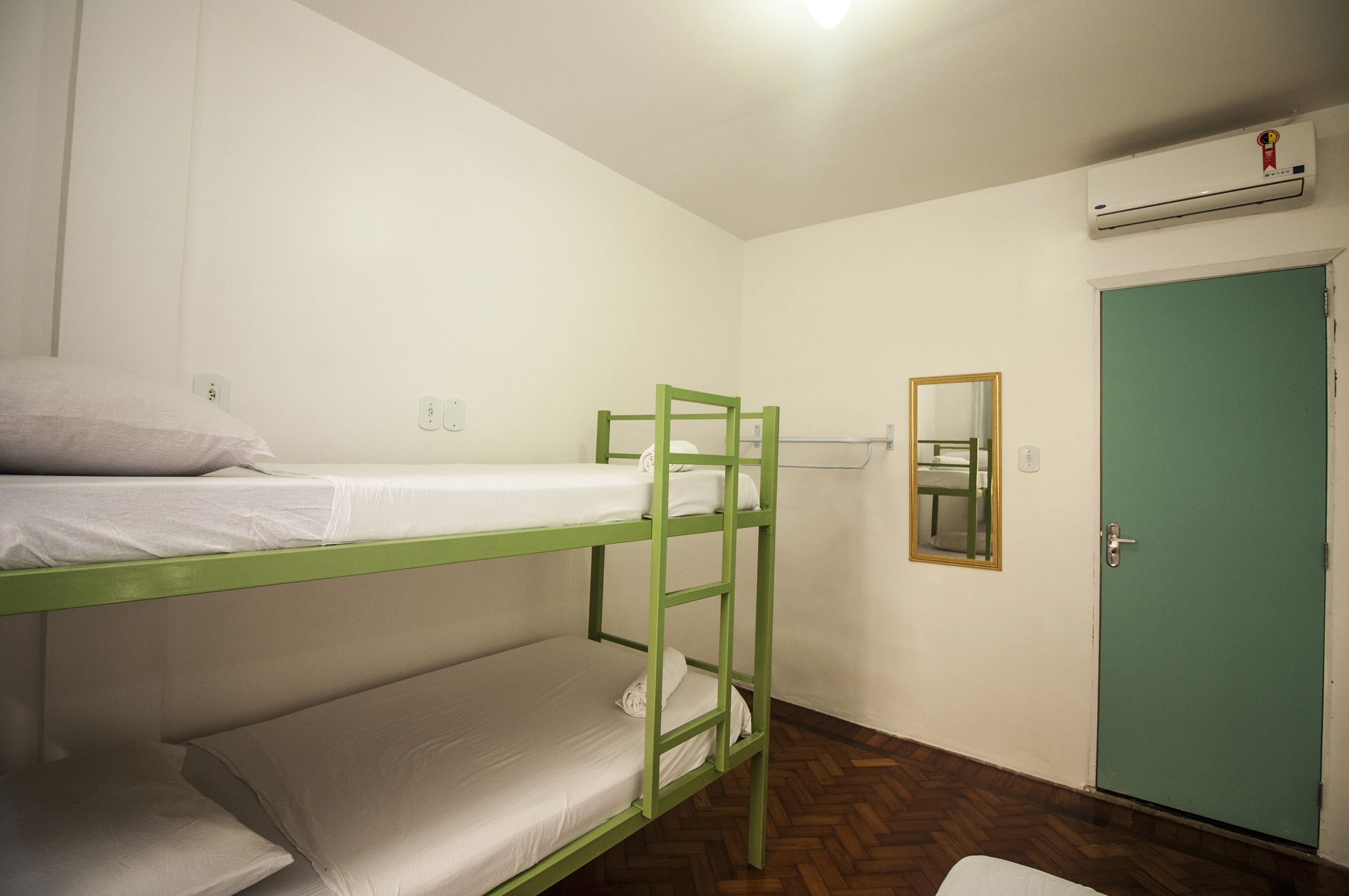 A bunk bed room with a green ladder, a green door, and a mirror on the wall.