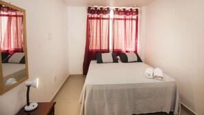 Un dormitorio con cama, espejo, lámpara y ventana con cortinas.