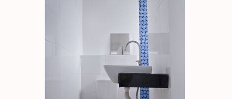 A bathroom with white tiles, a white sink, a blue-tiled shower wall, and a purple trash bin.