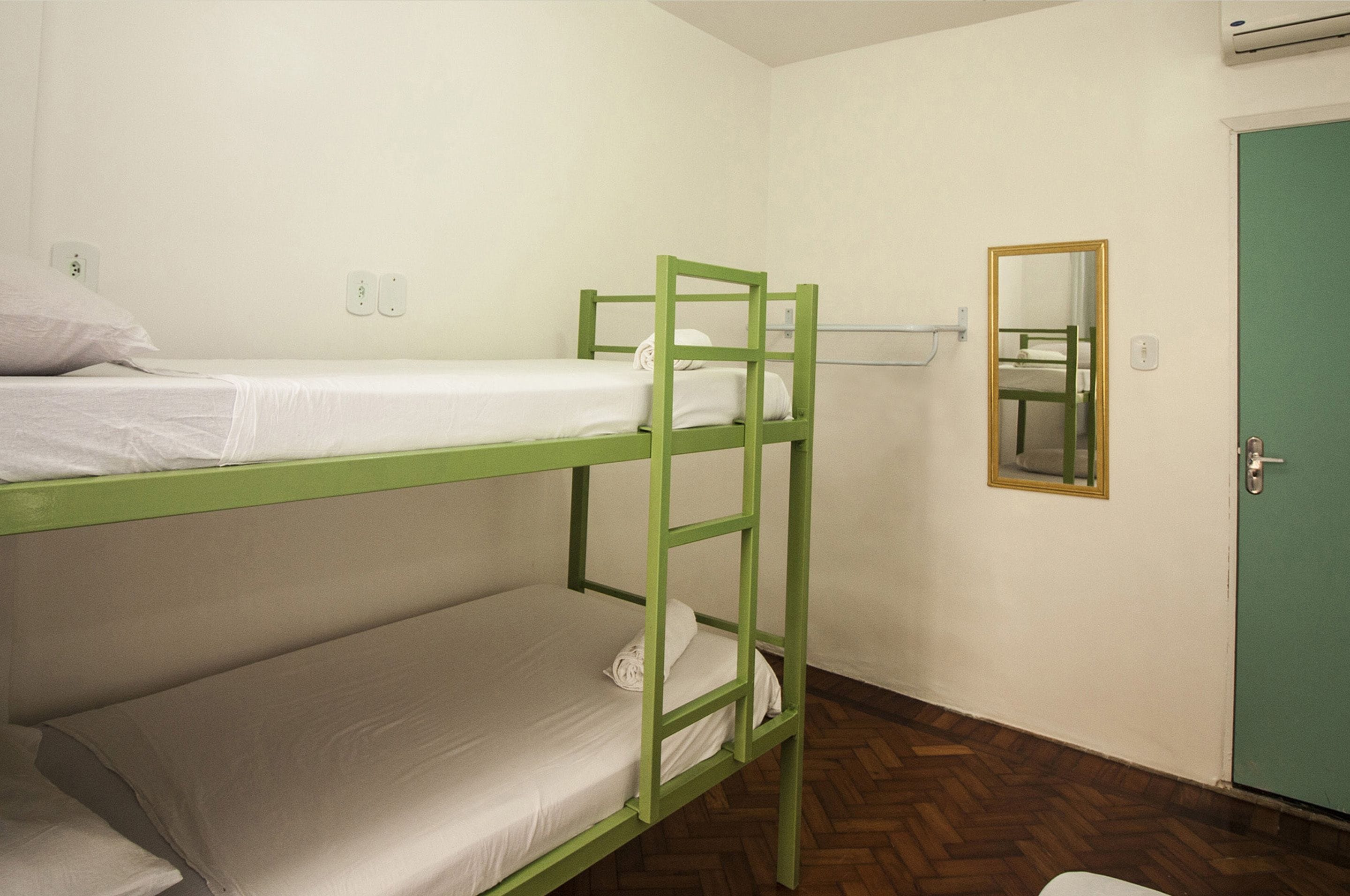 A bunk bed room with a green frame, white bedding, a mirror on the wall, and a green door.