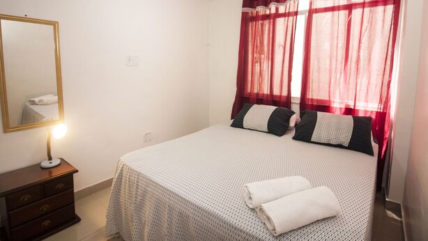 Una cama bien tendida con una colcha de diseño blanco y negro, una lámpara de noche y un espejo sobre un aparador.