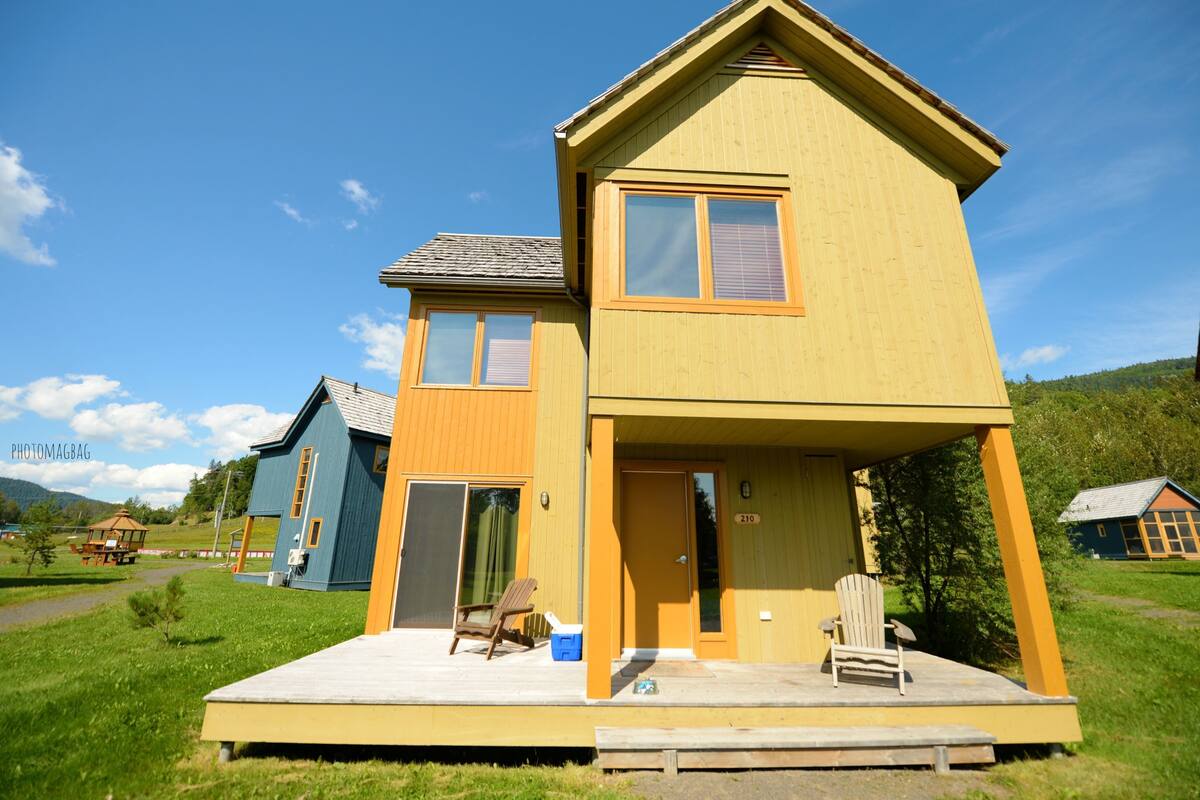 A two-story wooden house with a porch, a small deck, and a clear sky.