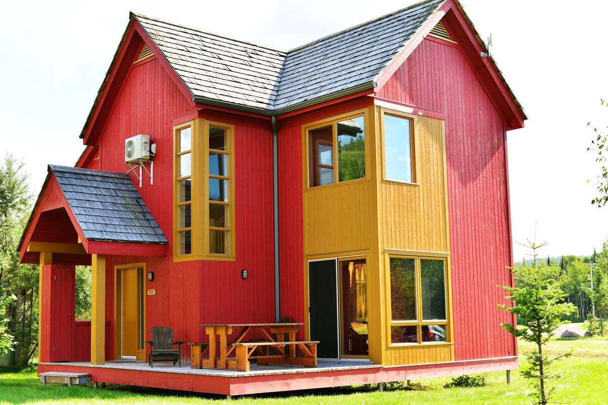 A red and yellow wooden house with a porch, a table, and a chair.