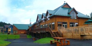 Un chalet en bois avec un toit vert, une terrasse couverte et un escalier menant à l’entrée.